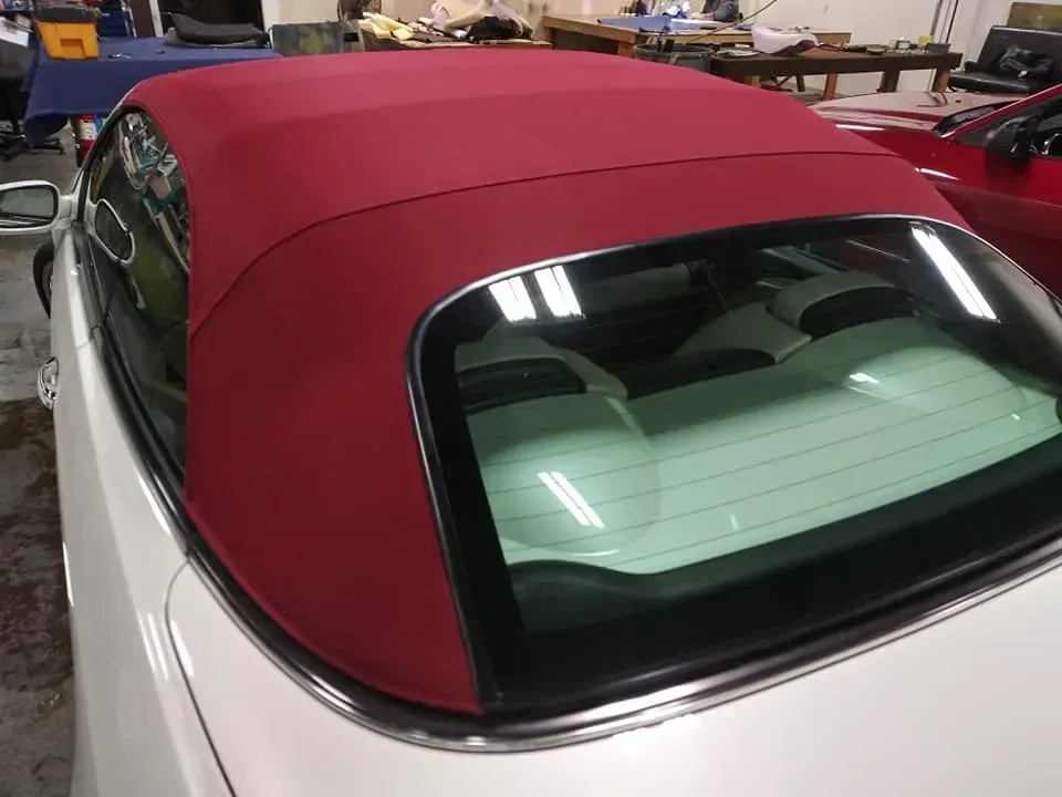 A red fabric convertible top on a white car, viewed from the rear, parked in an indoor garage.