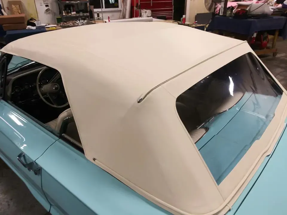 A close-up, high-angle view of a light blue classic convertible with a new tan fabric soft top in a garage setting.
