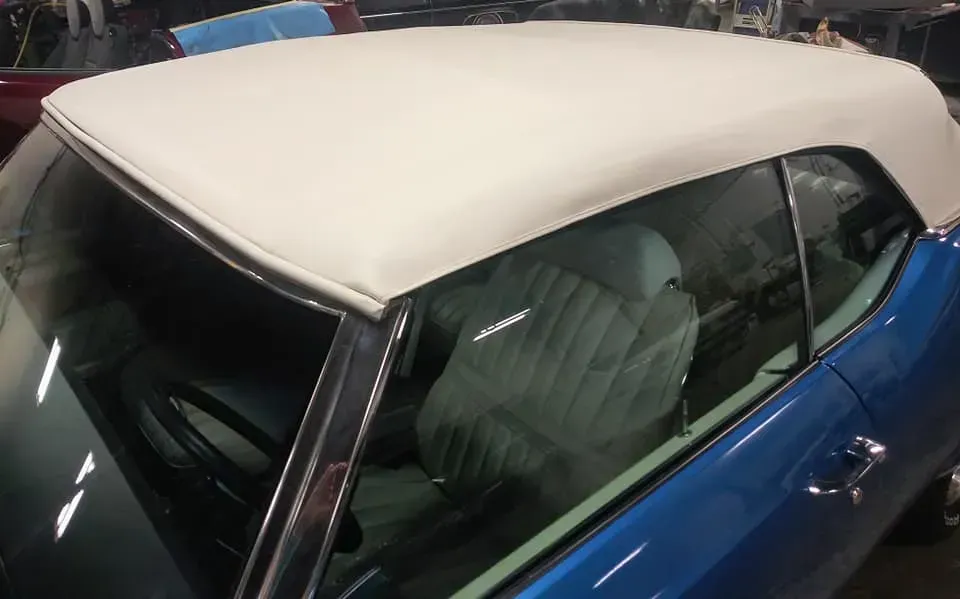 Close-up view of the front half of a blue vintage convertible car with a white fabric top, parked in a garage.