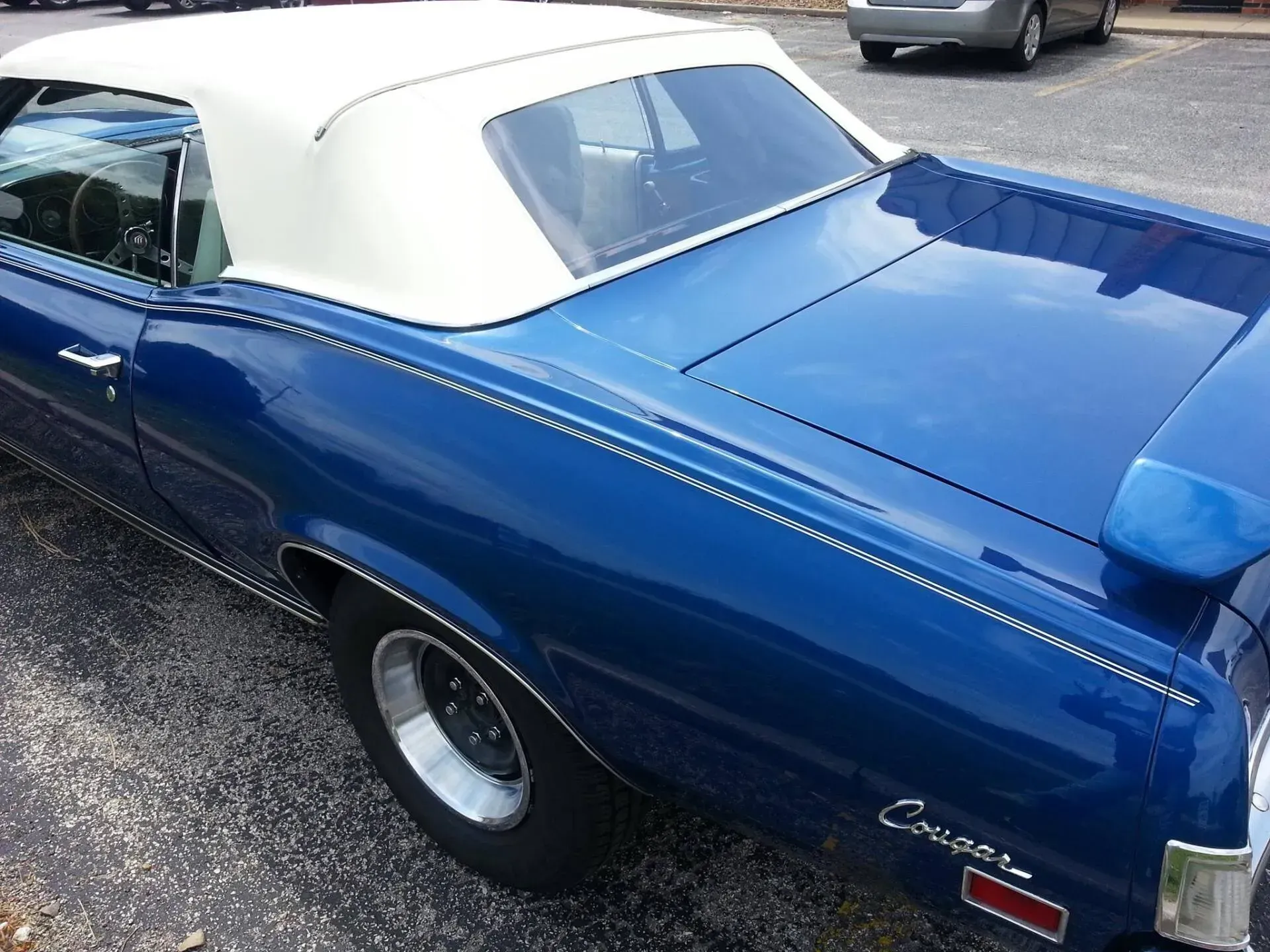 A blue vintage Mercury Cougar convertible with a white soft top, parked on an asphalt surface.