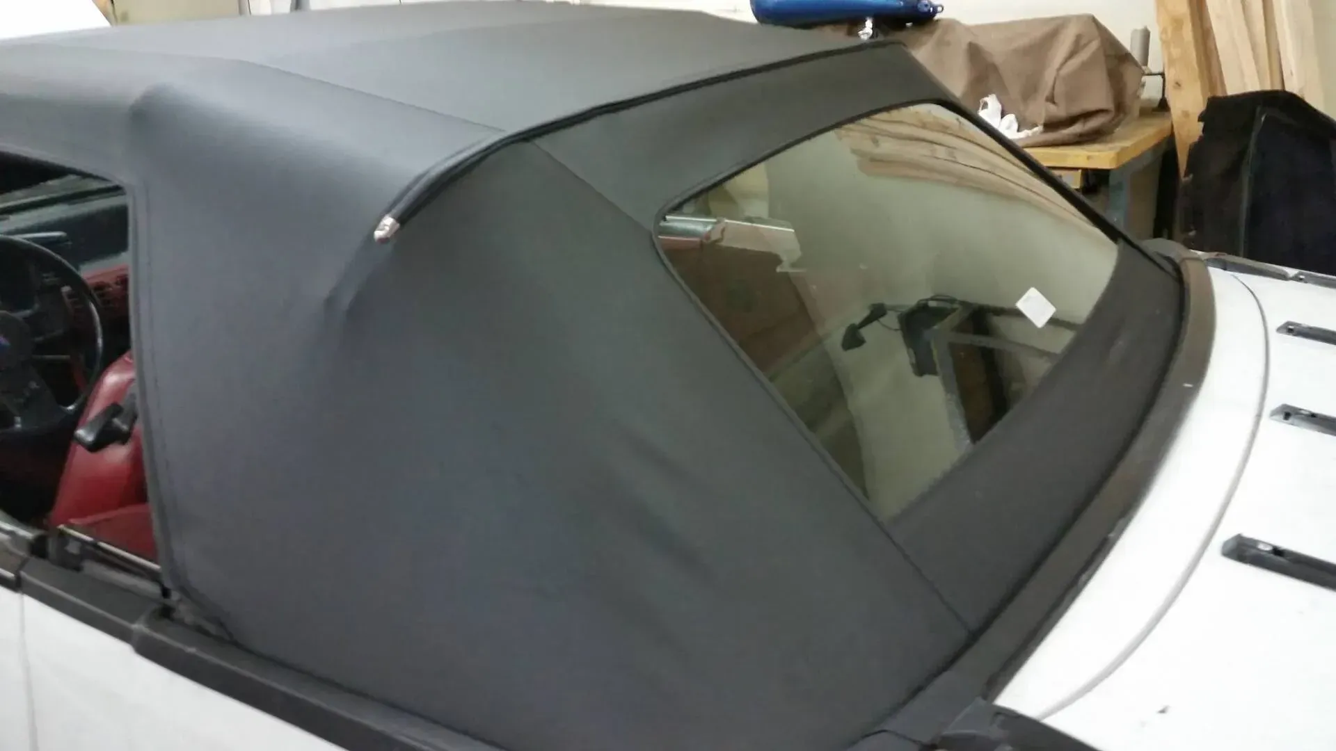 A black convertible soft top with a rear glass window installed on a white car inside a workshop.
