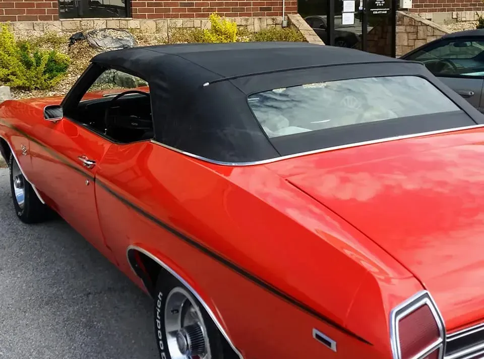 A bright orange vintage convertible car with a black top parked outside a brick building.