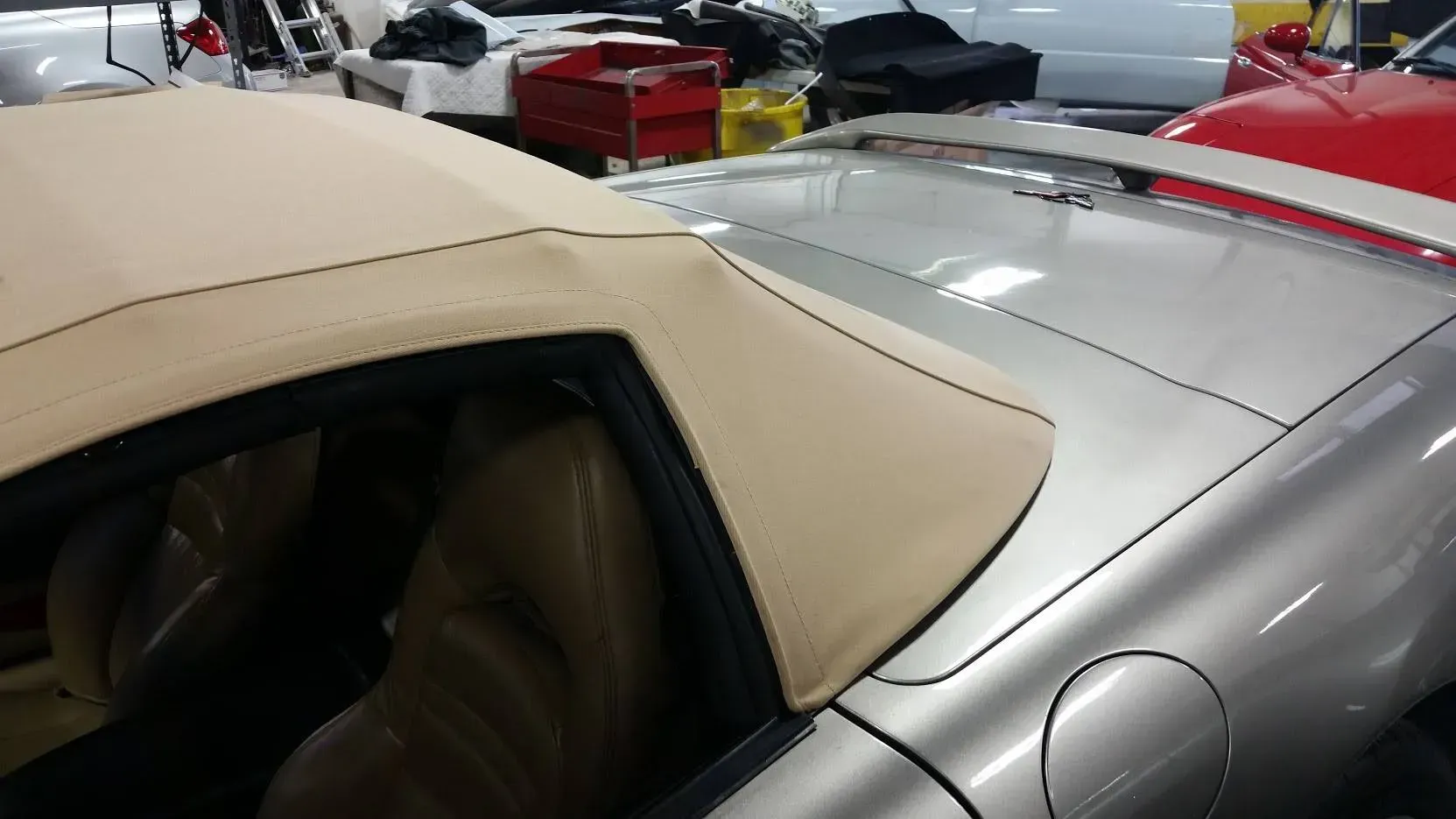 A tan convertible top on a silver car in a garage, focusing on the rear roof section and deck lid.