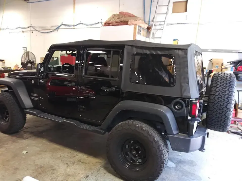 A black four-door Jeep Wrangler with a soft top parked inside a garage.