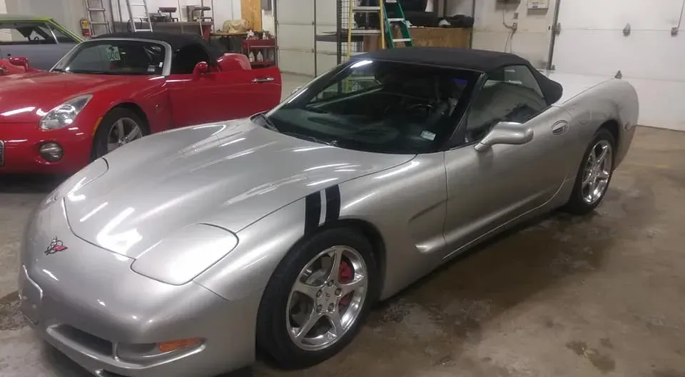 A silver convertible Chevrolet Corvette parked in a garage next to a red sports car.