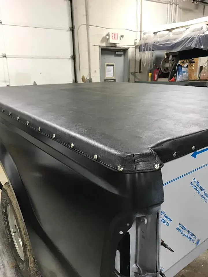 A black vinyl tonneau cover secured with metal snaps over a truck bed inside a garage.