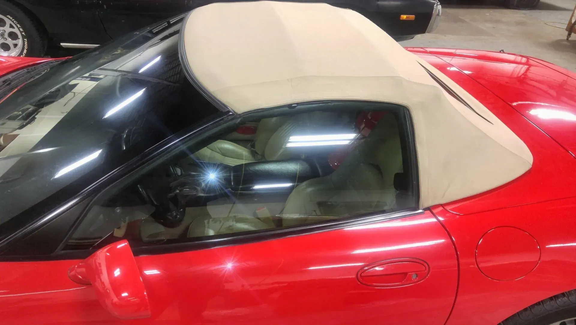 A close-up, high-angle shot of a red convertible car with a tan soft-top roof, parked in an indoor garage.