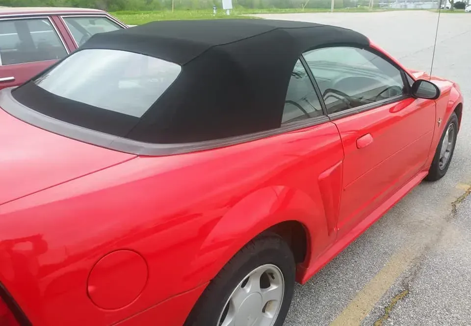 A vibrant red convertible with a black soft top parked on an asphalt lot.