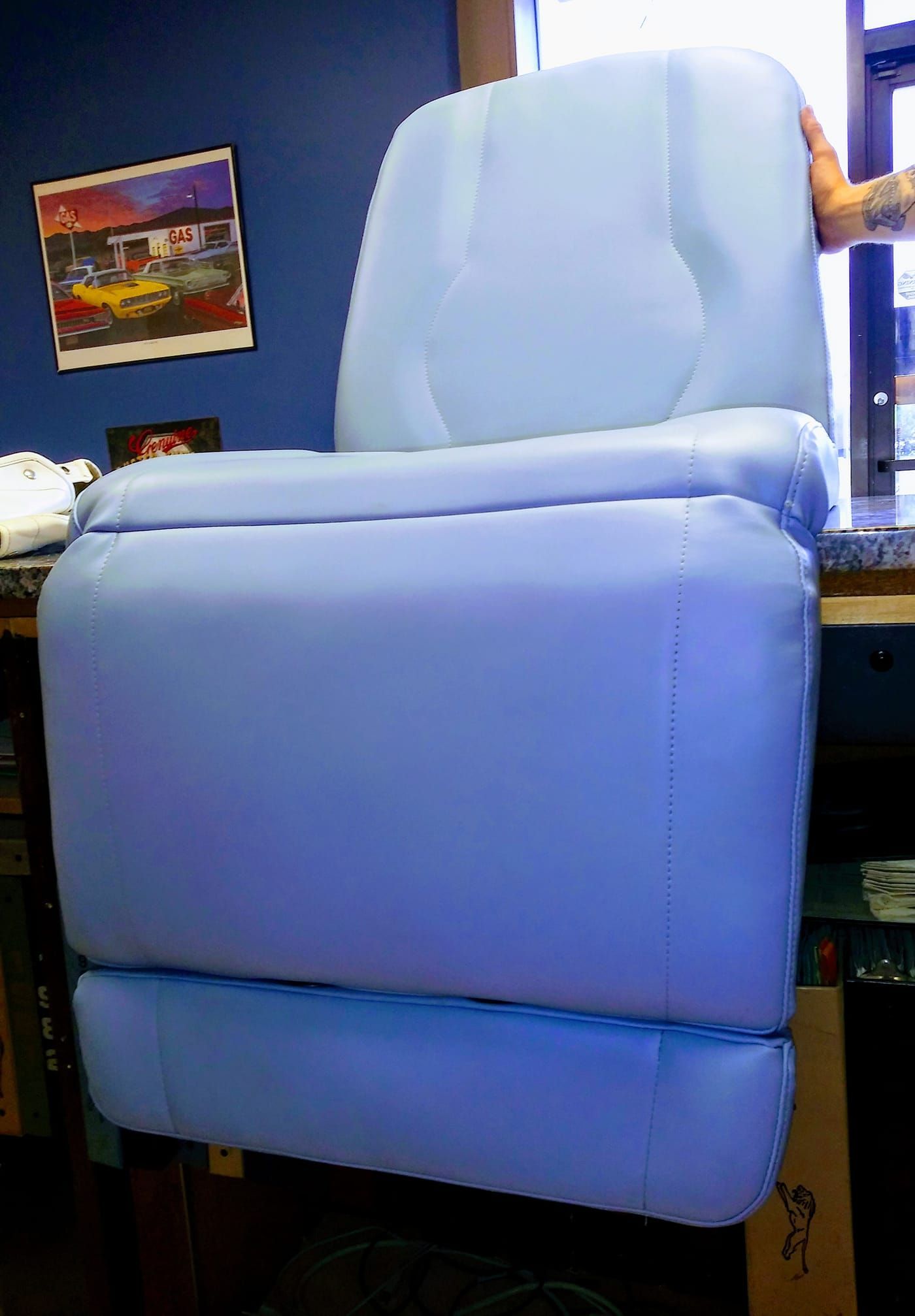 A person holding up a light blue upholstered recliner seat back in an office or studio setting.