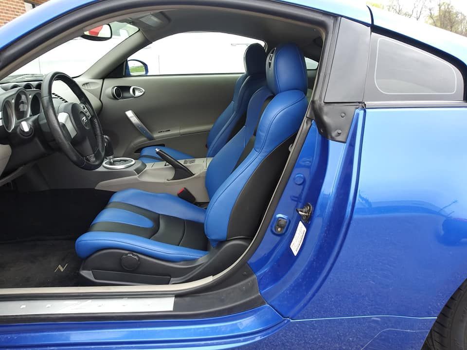 An open door reveals the interior of a blue sports car featuring blue and black leather bucket seats.