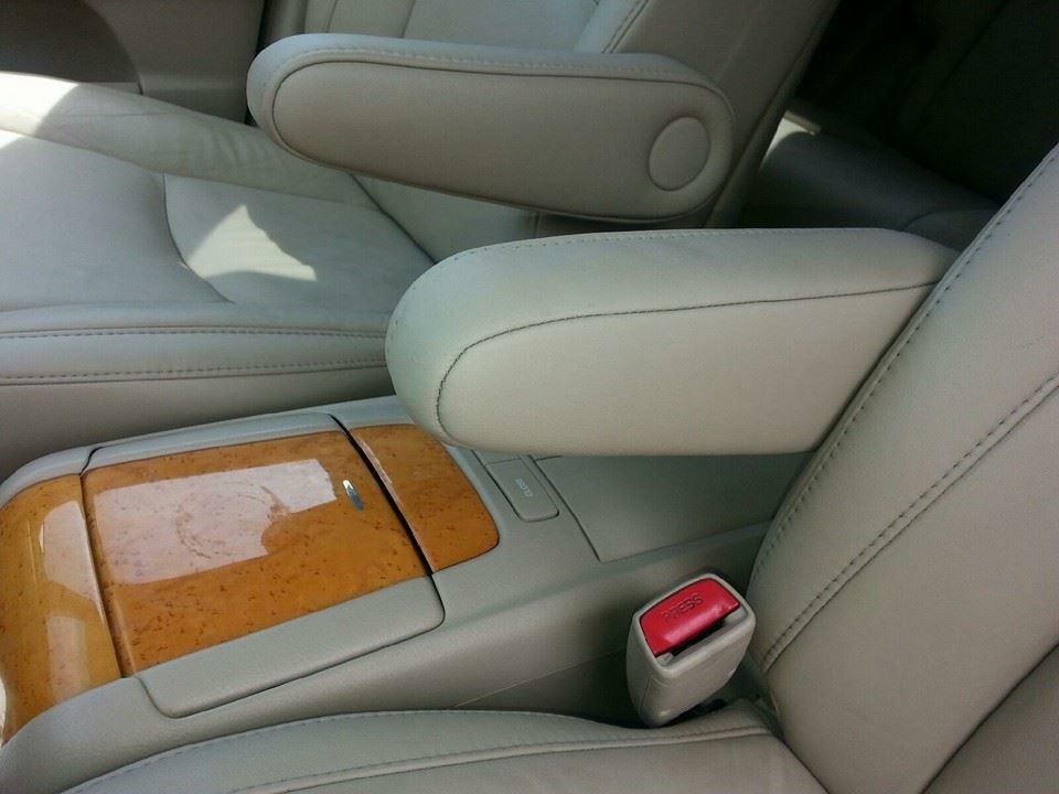 Close-up view of the center console and armrests of a car interior with beige leather seats and wood-grain trim.
