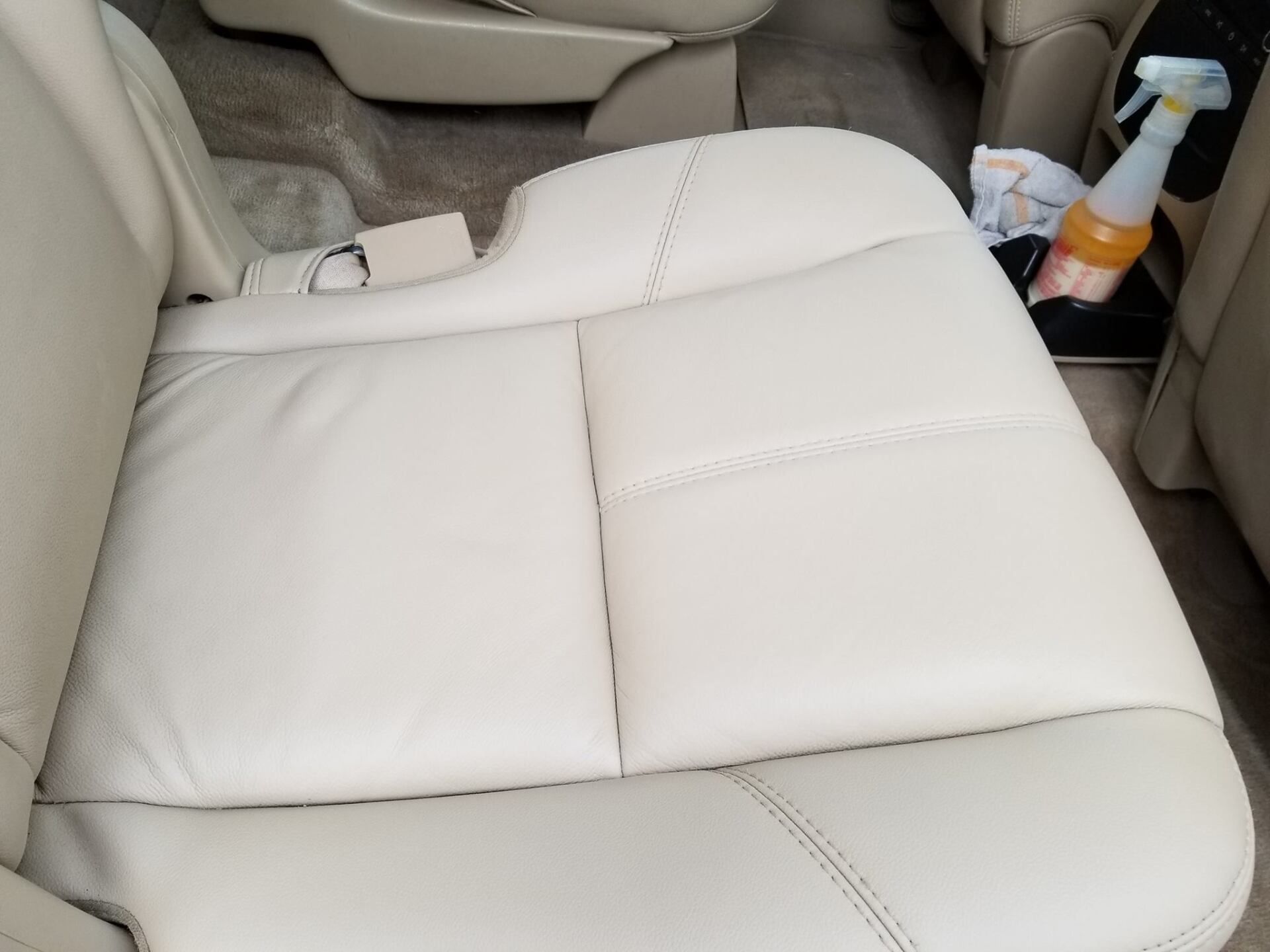 A beige leather car seat with a bottle of cleaning spray in the cup holder.