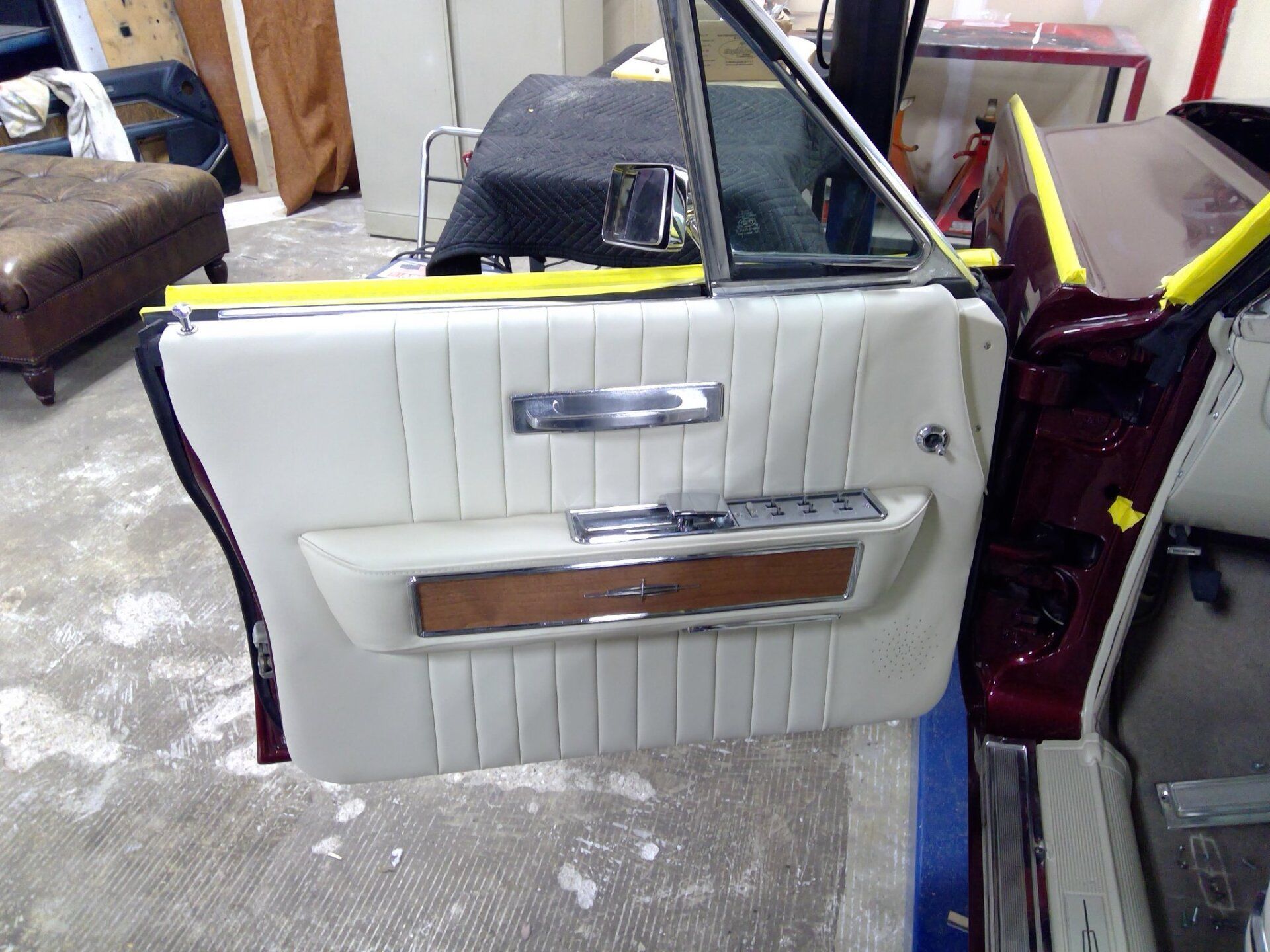 A close-up of a white, vintage car door interior panel with wood trim and chrome accents, set in a workshop.