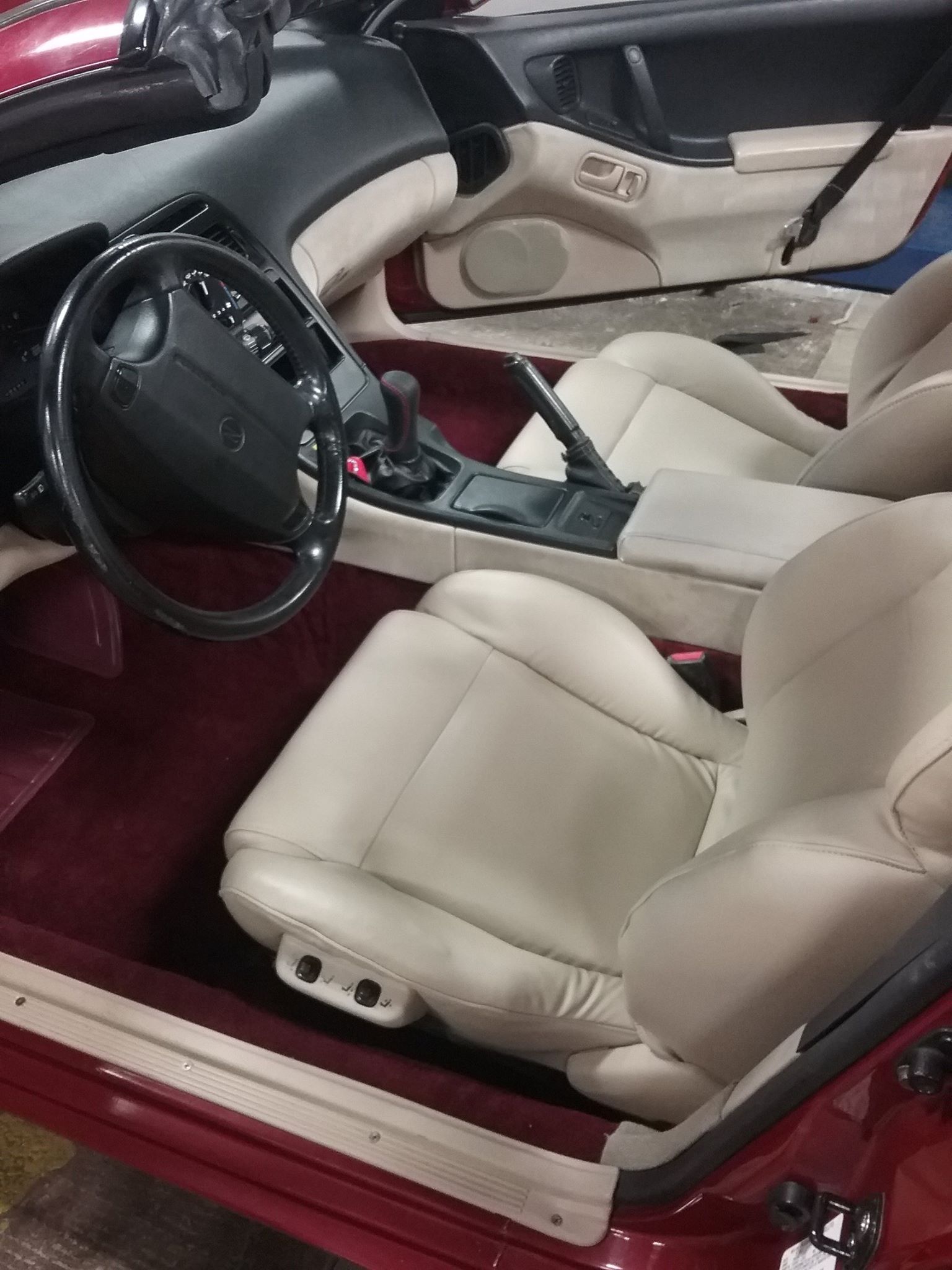 The interior of a red car featuring cream leather seats and a black dashboard with a manual transmission shifter.