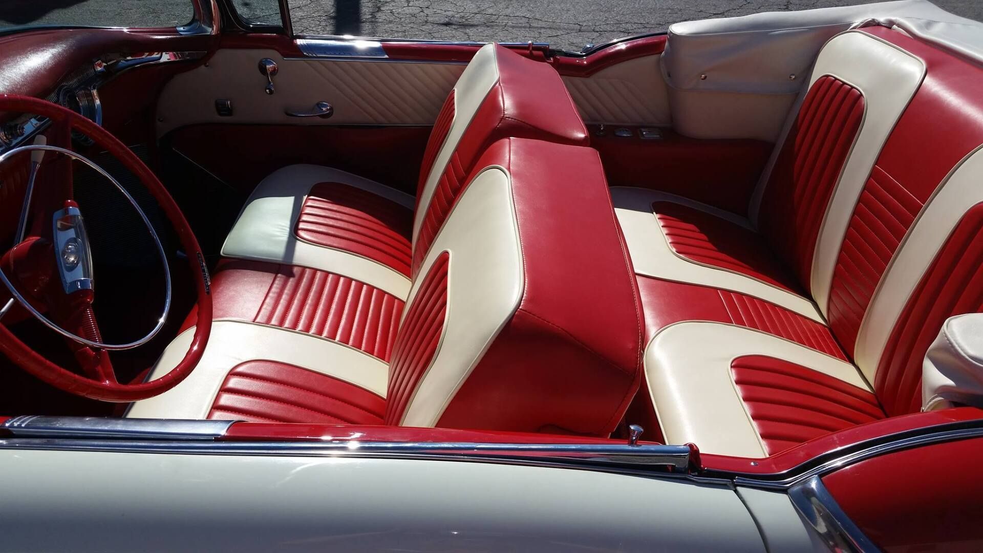 The interior of a classic convertible car with red and white leather bench seats and a matching steering wheel.