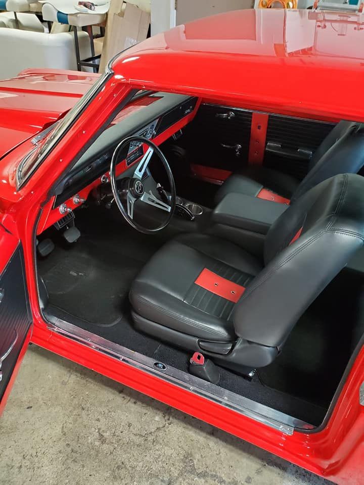 A bright red vintage car interior with black bucket seats featuring red center stripes and a three-spoke steering wheel.