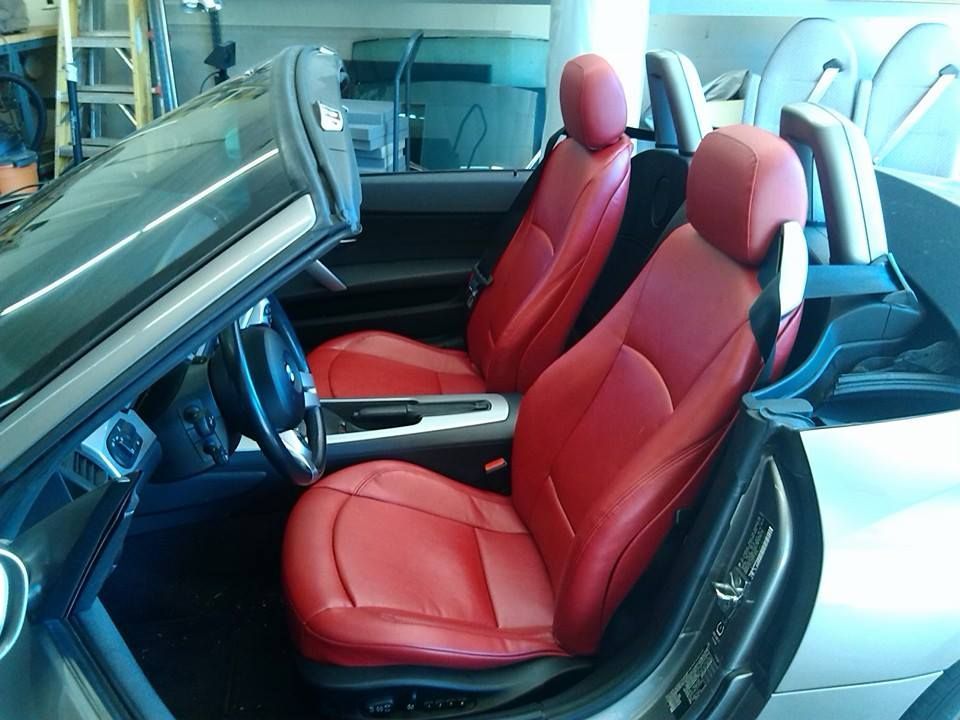 Interior of a convertible car with vibrant red leather seats, viewed from the open driver-side door in a garage setting.