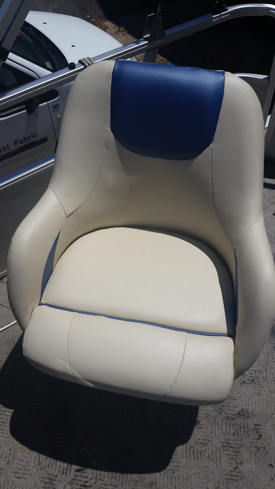 A beige marine helm seat with a blue textured headrest accent, positioned outdoors on a deck.