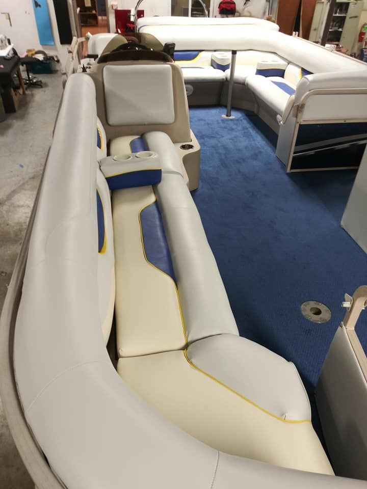 Interior of a boat with curved, beige, blue, and yellow upholstered bench seating over blue carpeting.