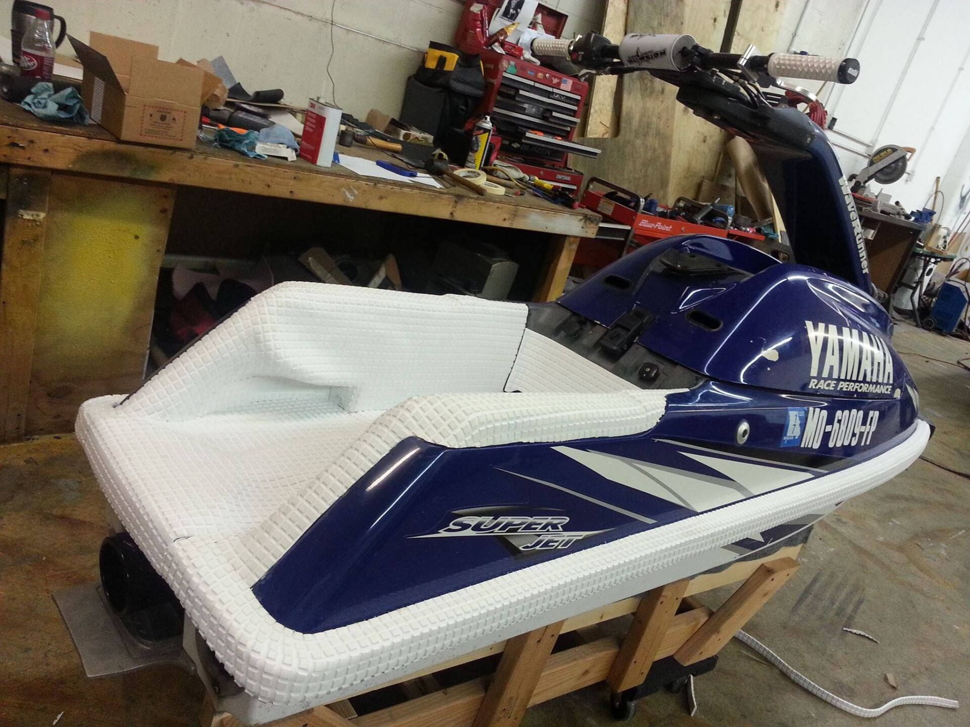 A blue and white Yamaha SuperJet stand-up personal watercraft sits on a wooden stand in a workshop.