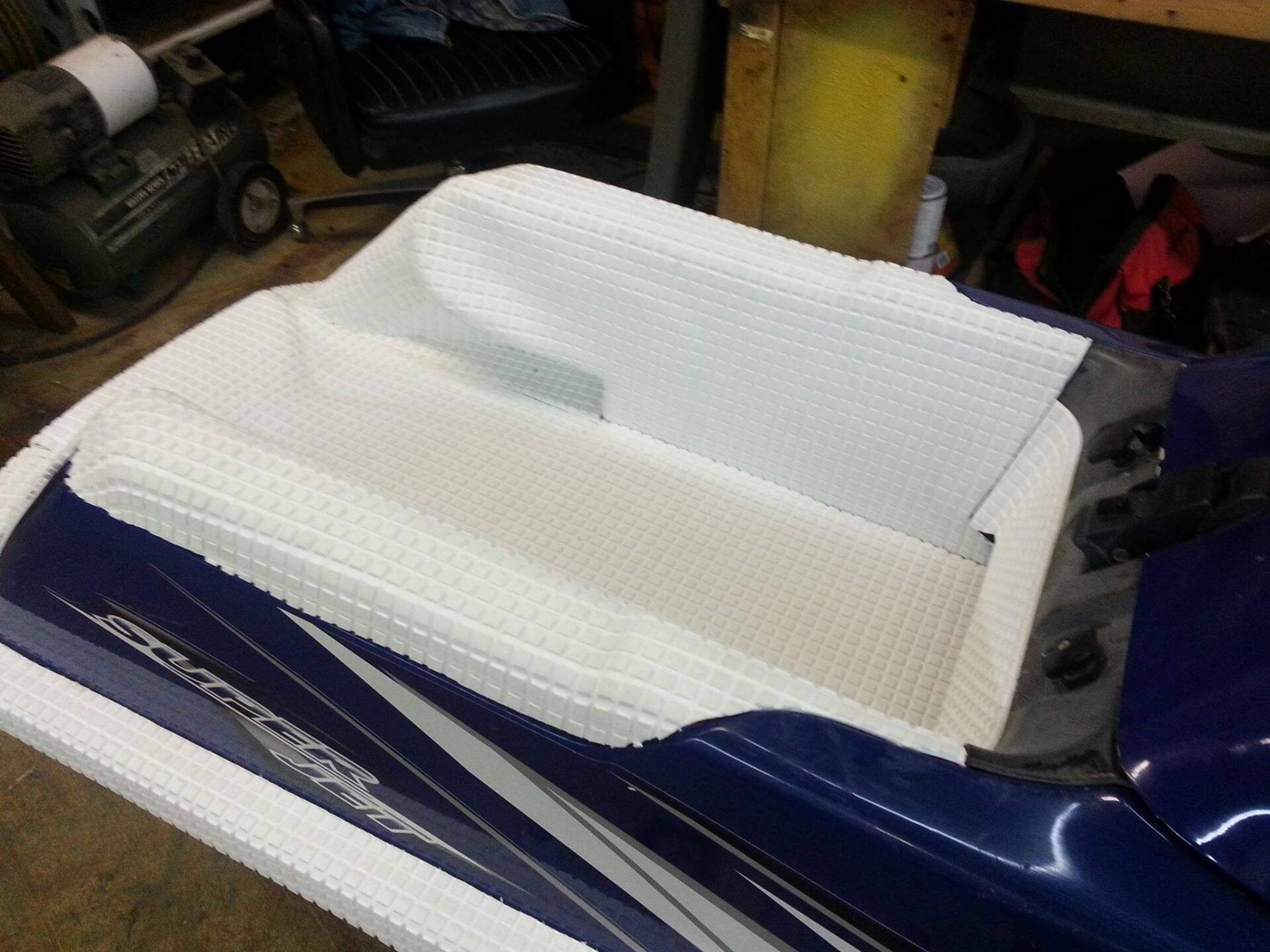 A textured, white, foam-like material fitted onto the blue deck and seat area of a personal watercraft in a workshop.