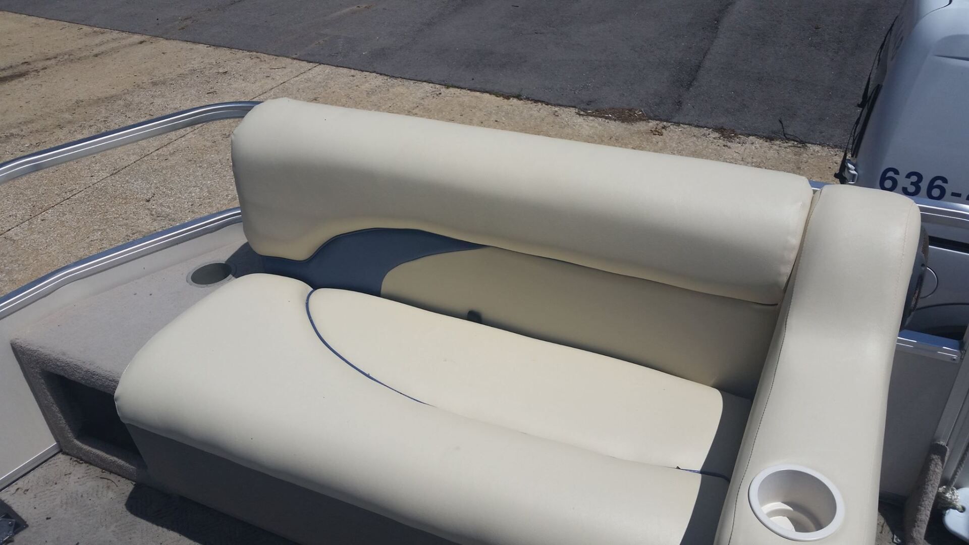A cream-colored pontoon boat seat with a built-in cup holder, set against a paved surface.