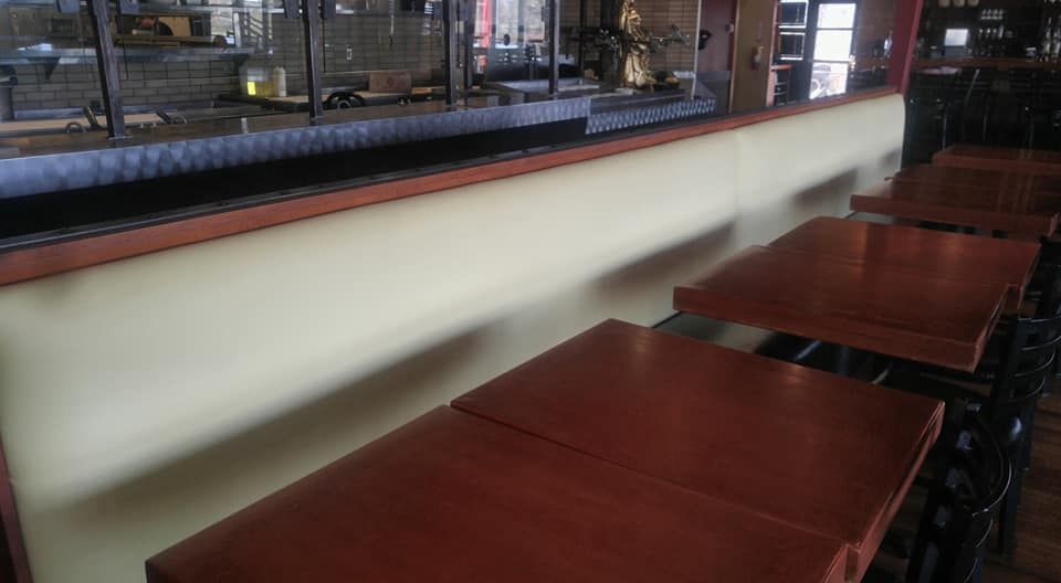 A row of square wooden tables next to a long, beige upholstered booth seat in a restaurant setting.