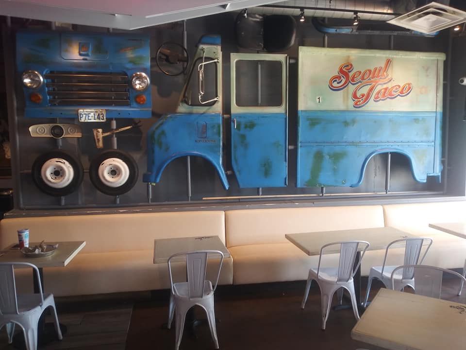 A restaurant wall decorated with a blue food truck model above white booths and tables with chairs.