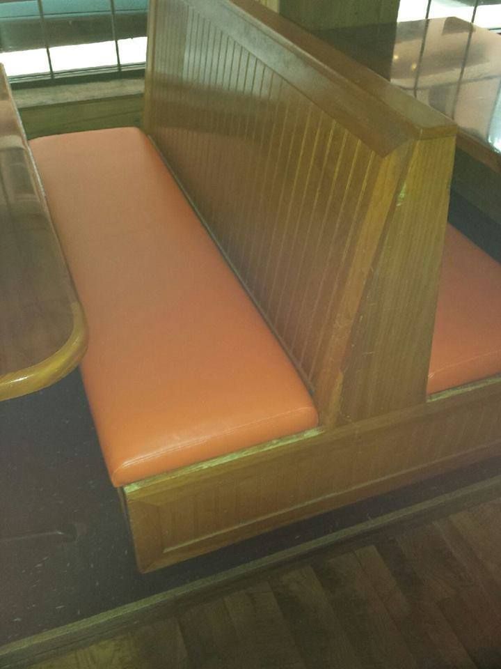 A wooden restaurant booth with orange vinyl seating in a dining area.