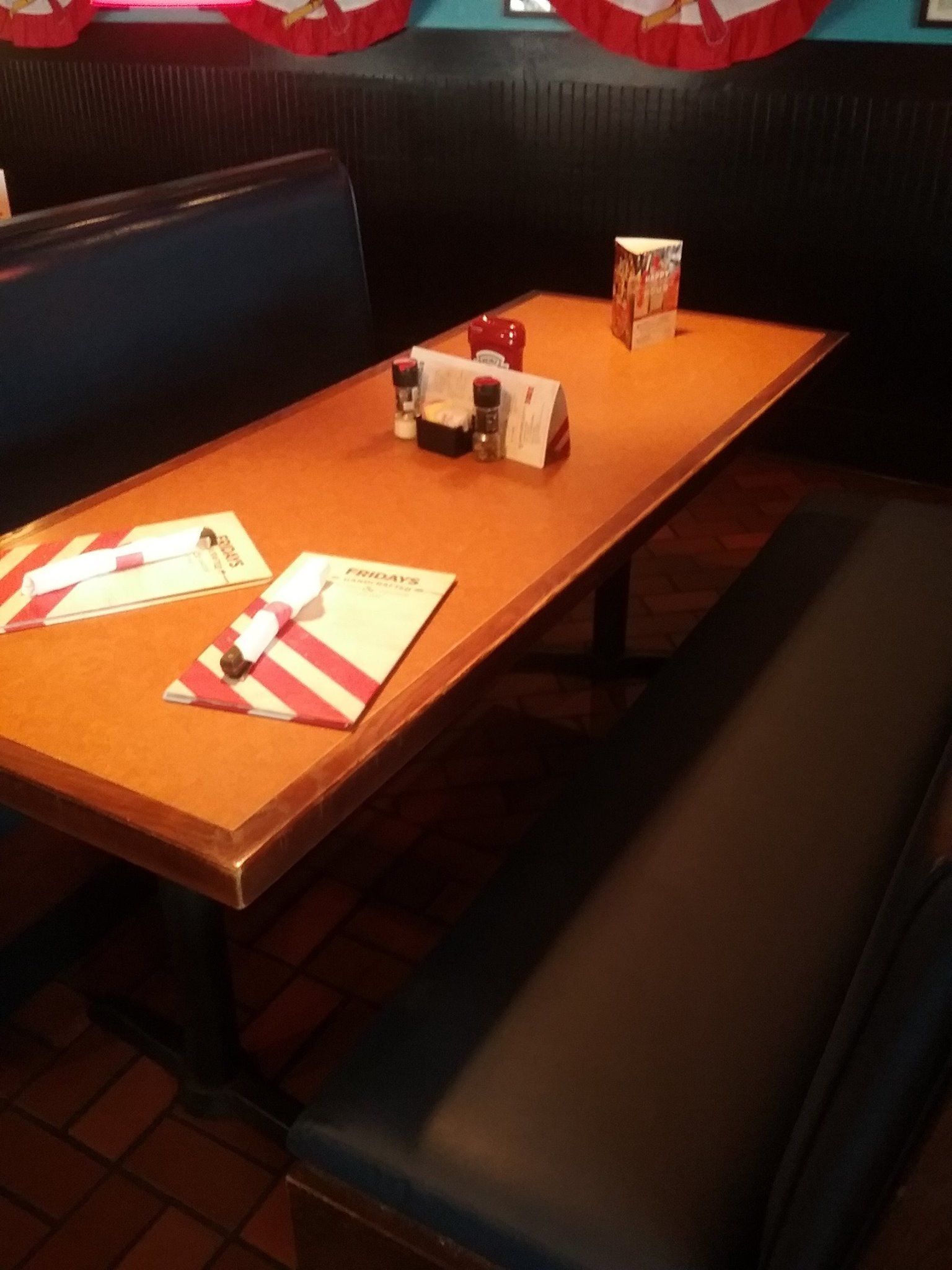 A table in a restaurant booth with orange tabletops, menus, and salt and pepper shakers.