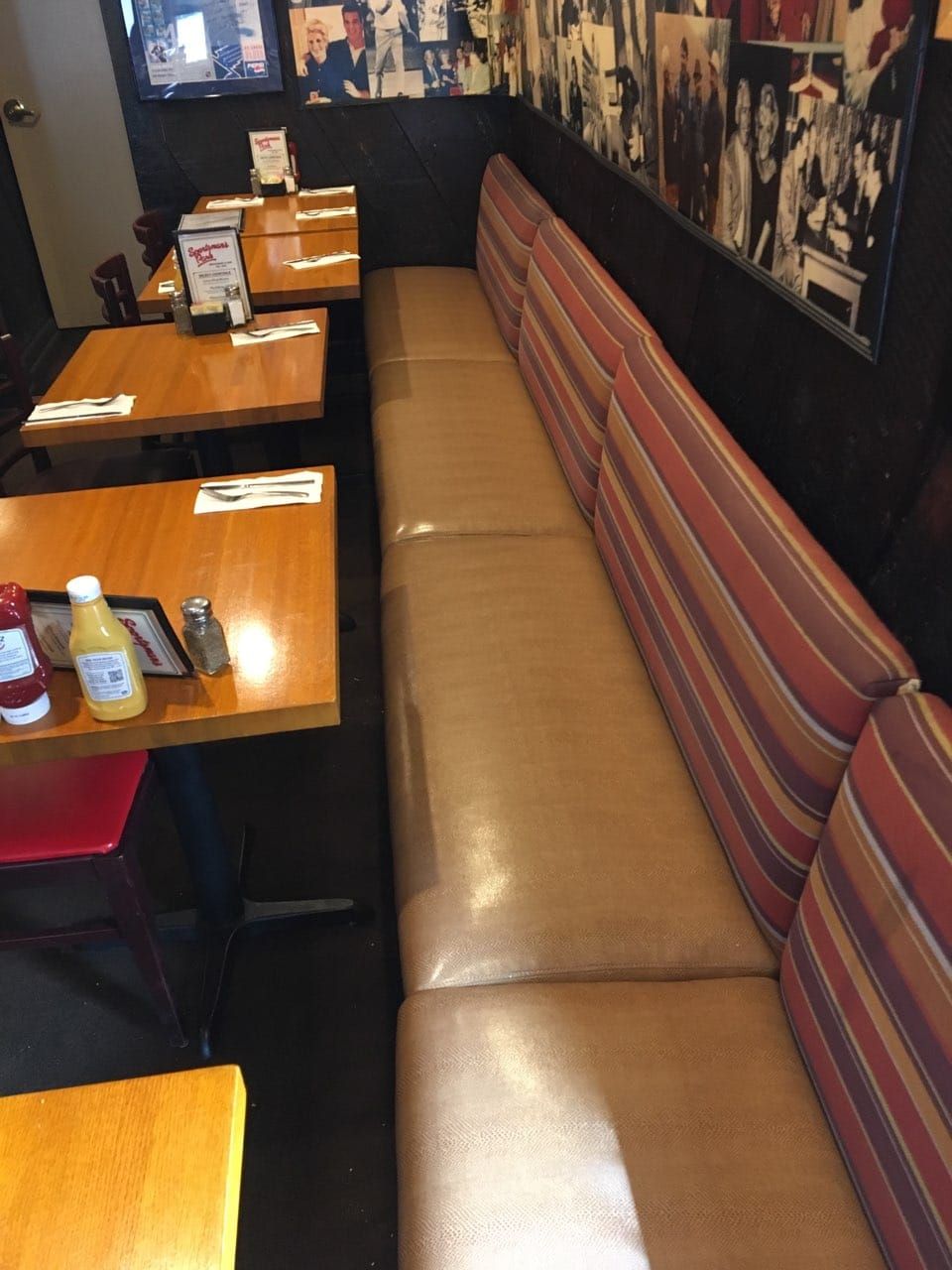 A row of wooden tables with striped booths along a dark wall decorated with black-and-white photographs.