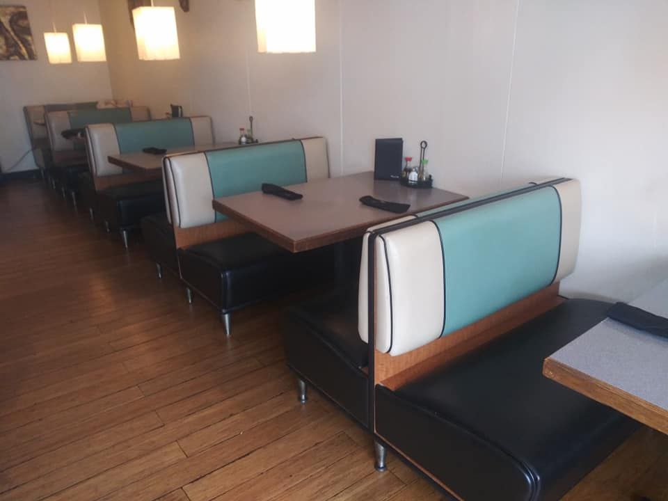 A row of diner-style booths with cream and teal upholstery and wooden tables in a restaurant with wood floors.