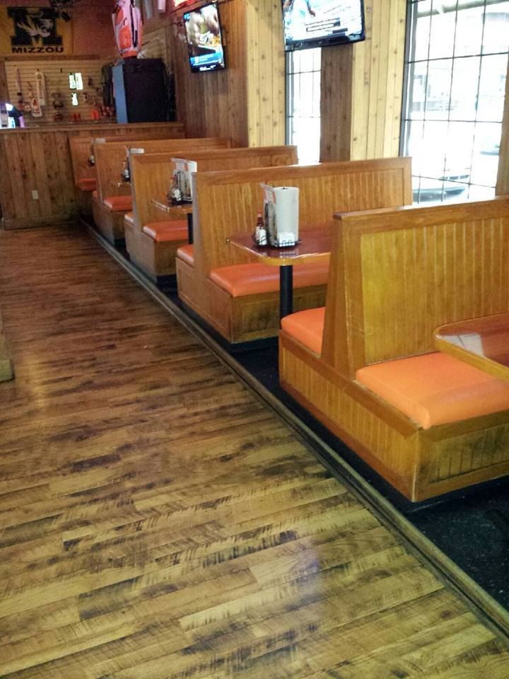 A row of wooden booths with orange cushions inside a casual, rustic-style restaurant.