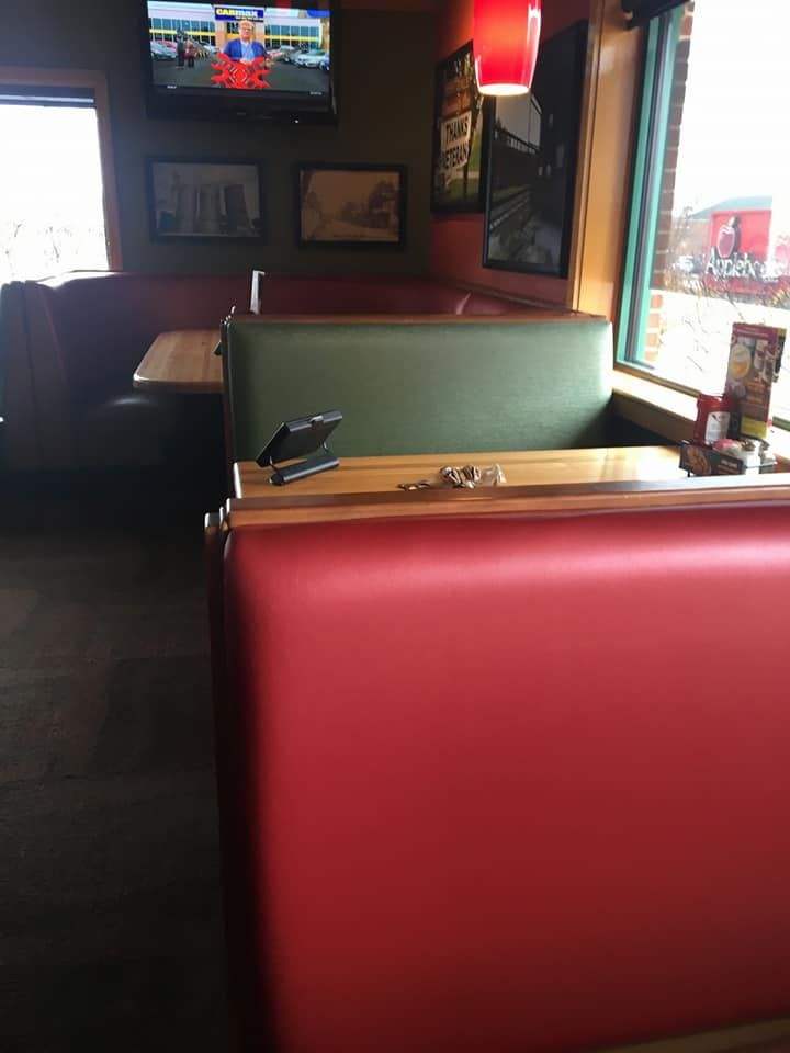 A restaurant dining area featuring red and green vinyl booths, wooden tables, framed wall art, and a mounted television.