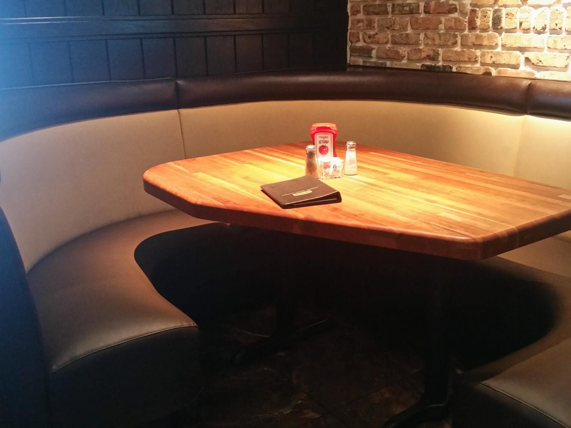 A curved beige and dark brown leather booth surrounds a wooden table with condiments and a menu in a restaurant.