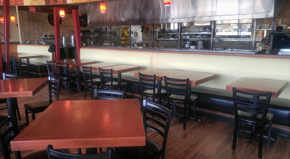 Empty tables and chairs in a restaurant dining area with a long banquette seating along a wooden service counter.