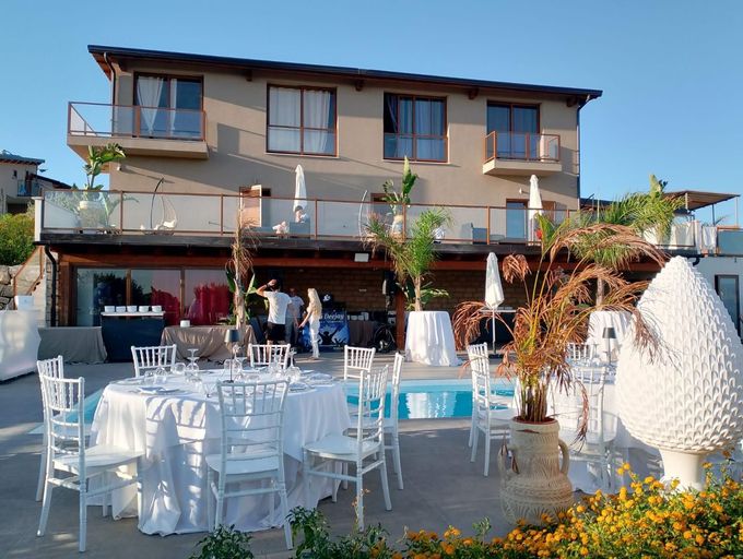 Allestimento per evento all'aperto con tavoli bianchi, sedie e decorazioni vicino a un edificio con piscina.