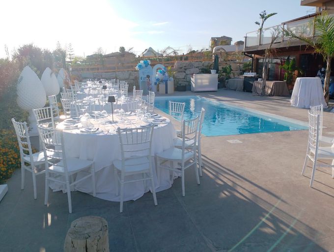 Allestimento per eventi all'aperto con tavoli rotondi, sedie bianche e piscina.