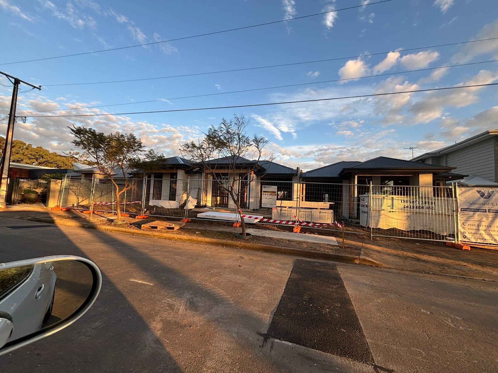 Construction site of new homes under a blue sky, with fencing and building materials visible.