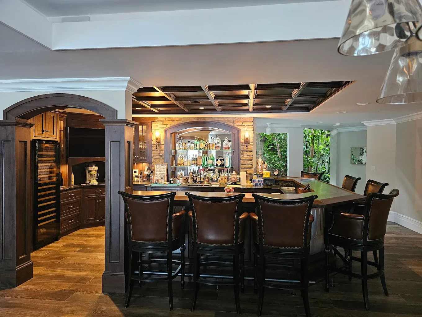 Basement bar with dark wood cabinets, brick backdrop, bar stools, and bottles.