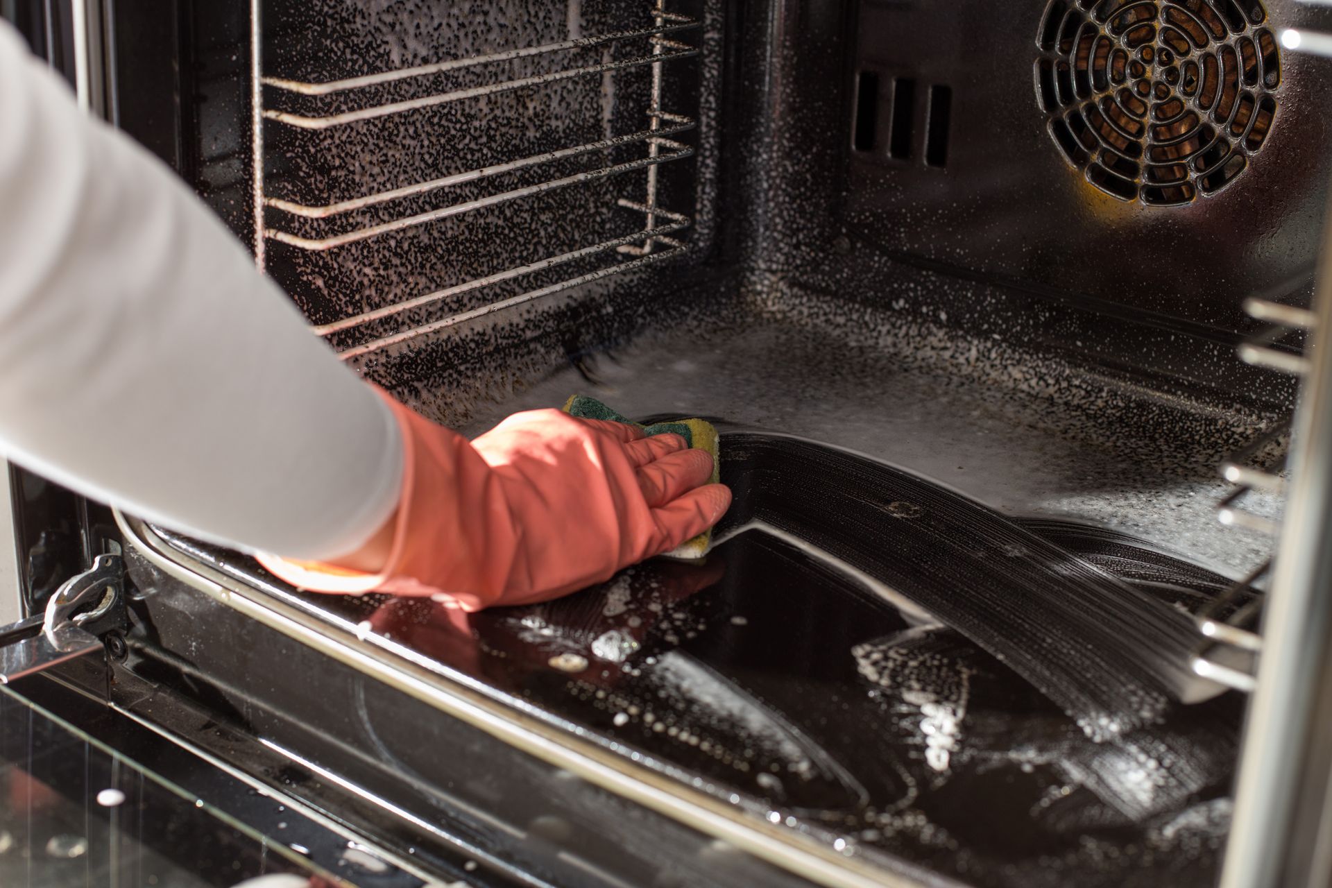 Person wearing red gloves cleaning inside an oven with a sponge.