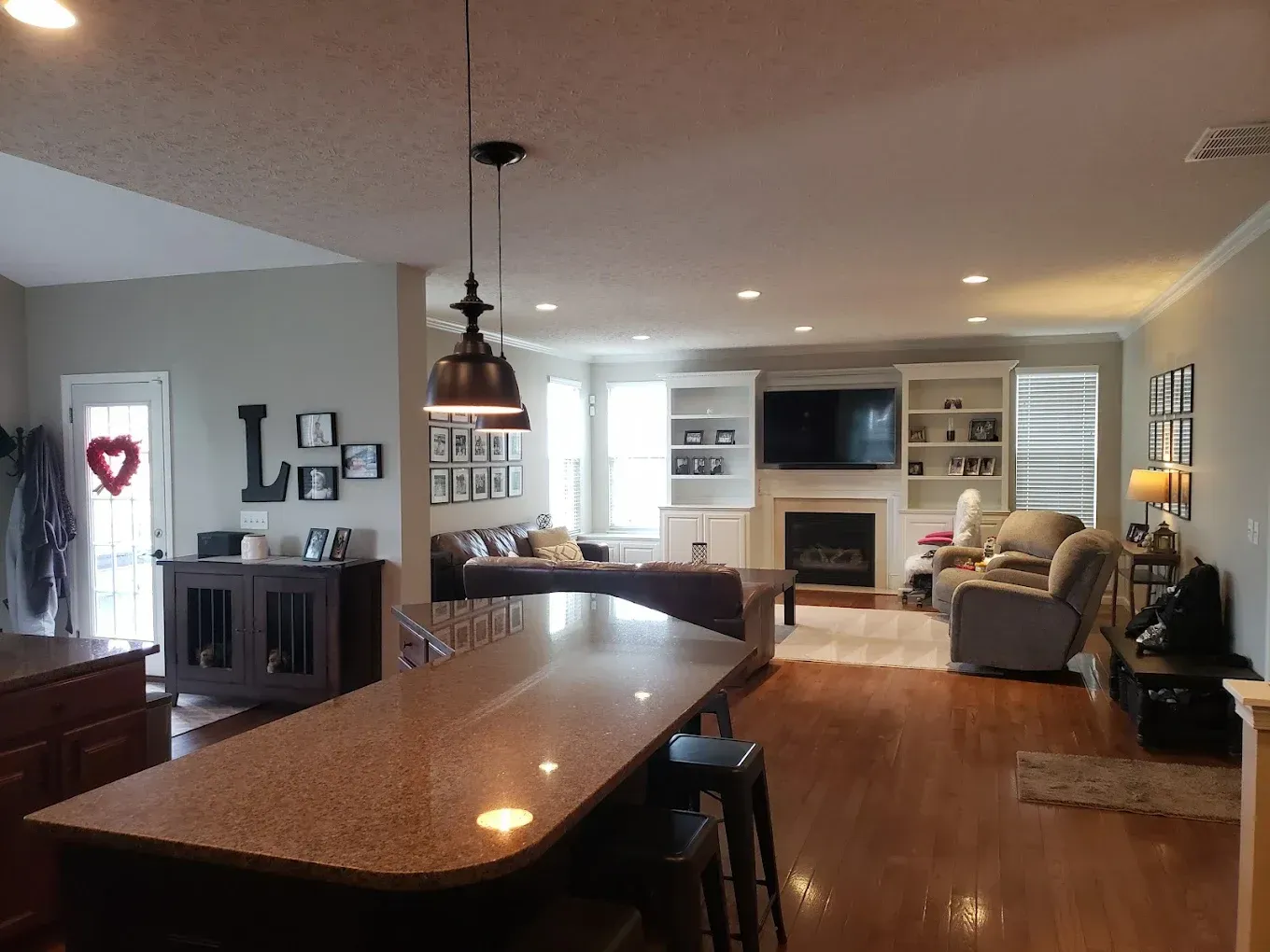 Open-concept living space with a kitchen island, living room with fireplace, and dark brown wood flooring.