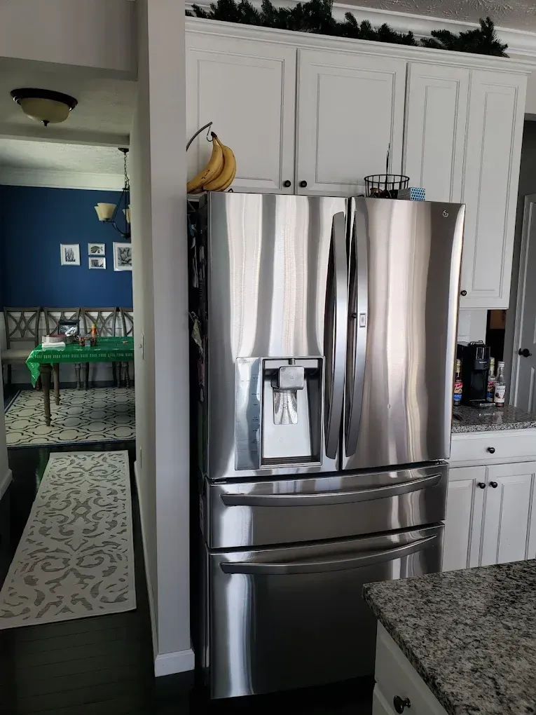Stainless steel refrigerator in a white kitchen, with a glimpse of a dining room with a blue wall.
