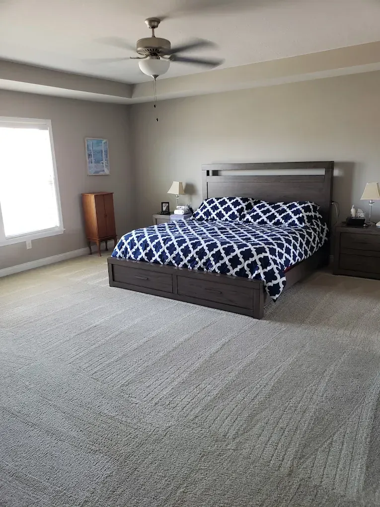 Bedroom with gray bed frame, blue patterned bedding, nightstands, and beige carpet.