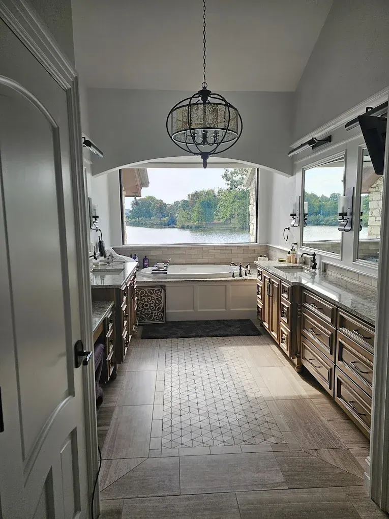 Bathroom with long vanity, stone floor, large window overlooking a lake, and chandelier.
