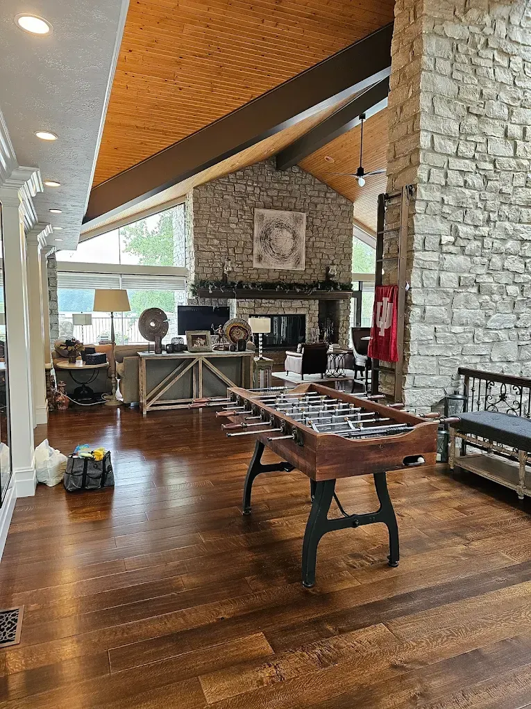 Spacious living room with a foosball table, stone fireplace, wood floor, and high, angled ceiling.