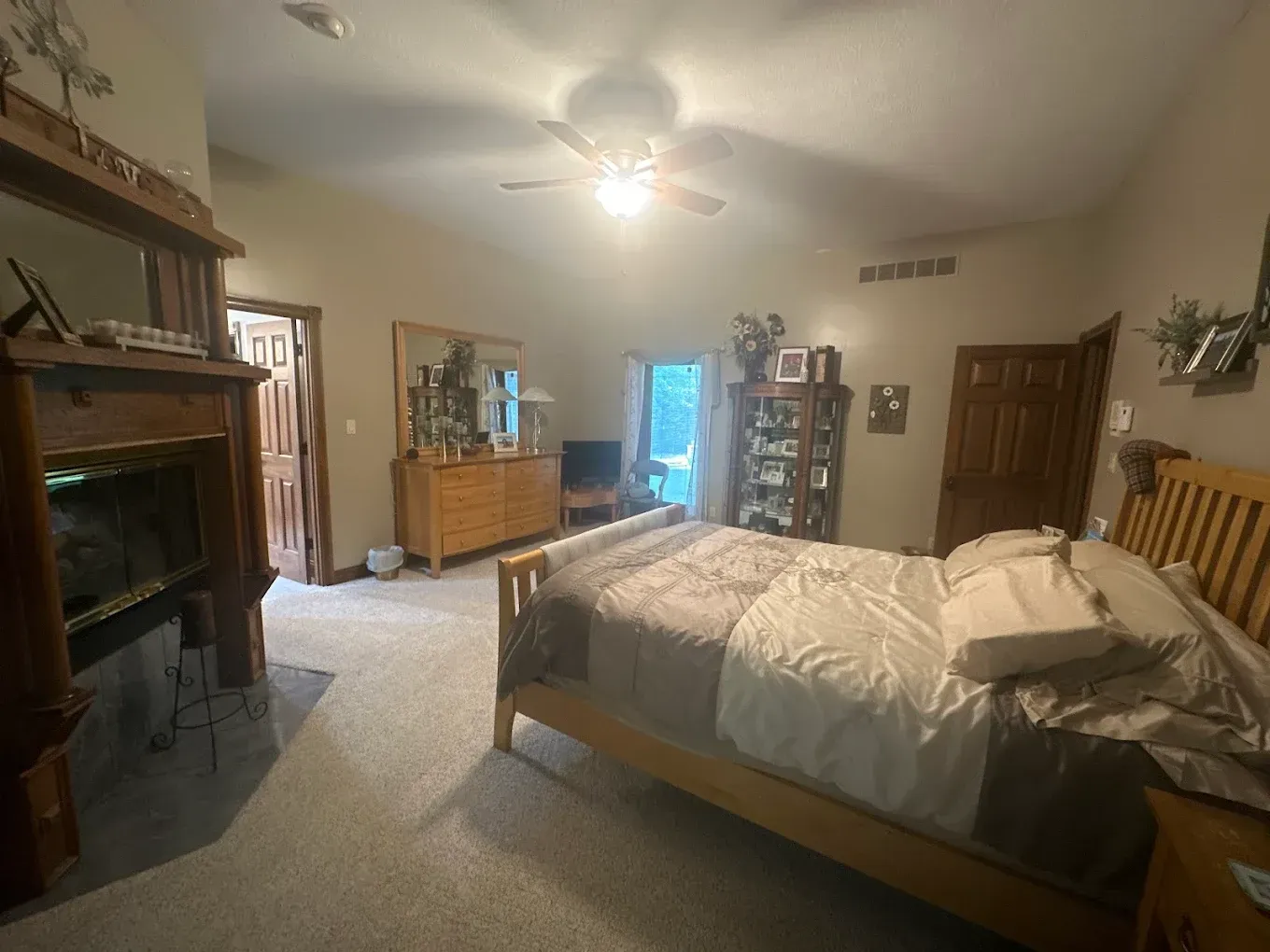 Bedroom with wooden furniture, fireplace, and bed. Neutral color scheme, vaulted ceiling, and natural light from a doorway.