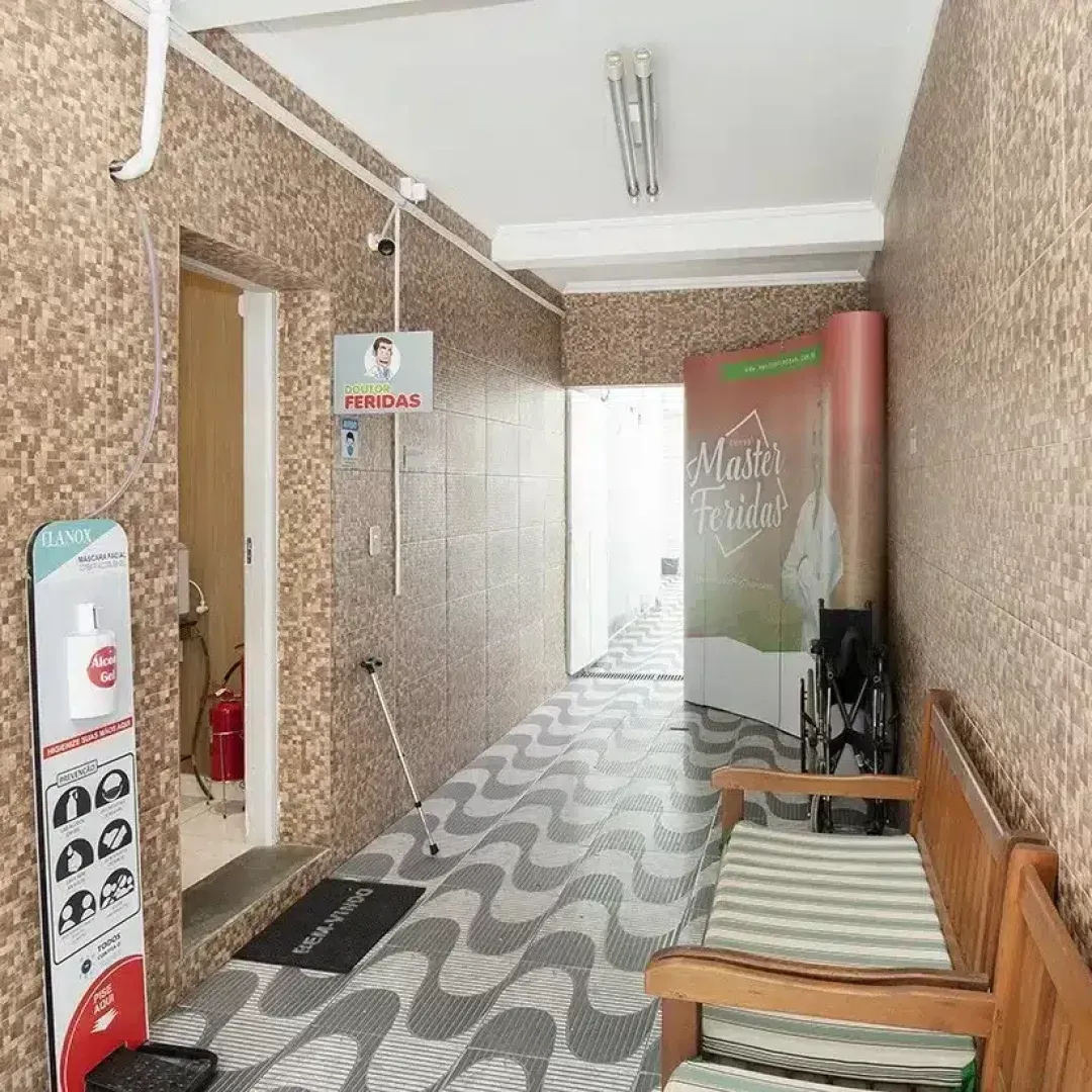 Corredor interno estreito com piso de ladrilho estampado, bancos, paredes revestidas com azulejos e uma porta no final.