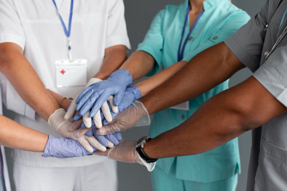 Equipe médica empilhando mãos enluvadas em um ambiente hospitalar.