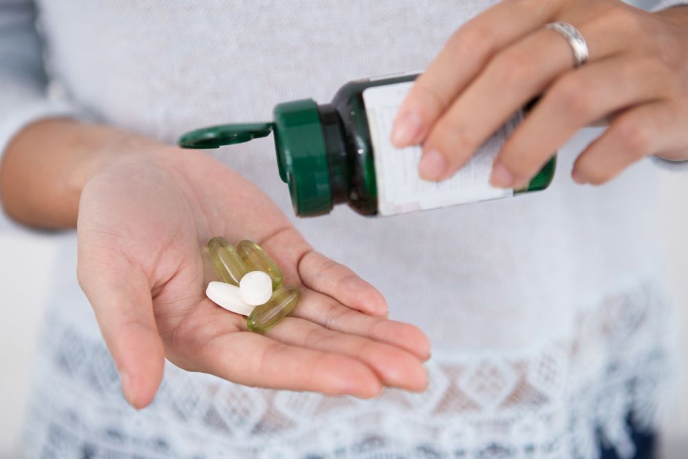Mãos despejando o conteúdo de uma garrafa verde na palma da mão, que contém pétalas de flores brancas.